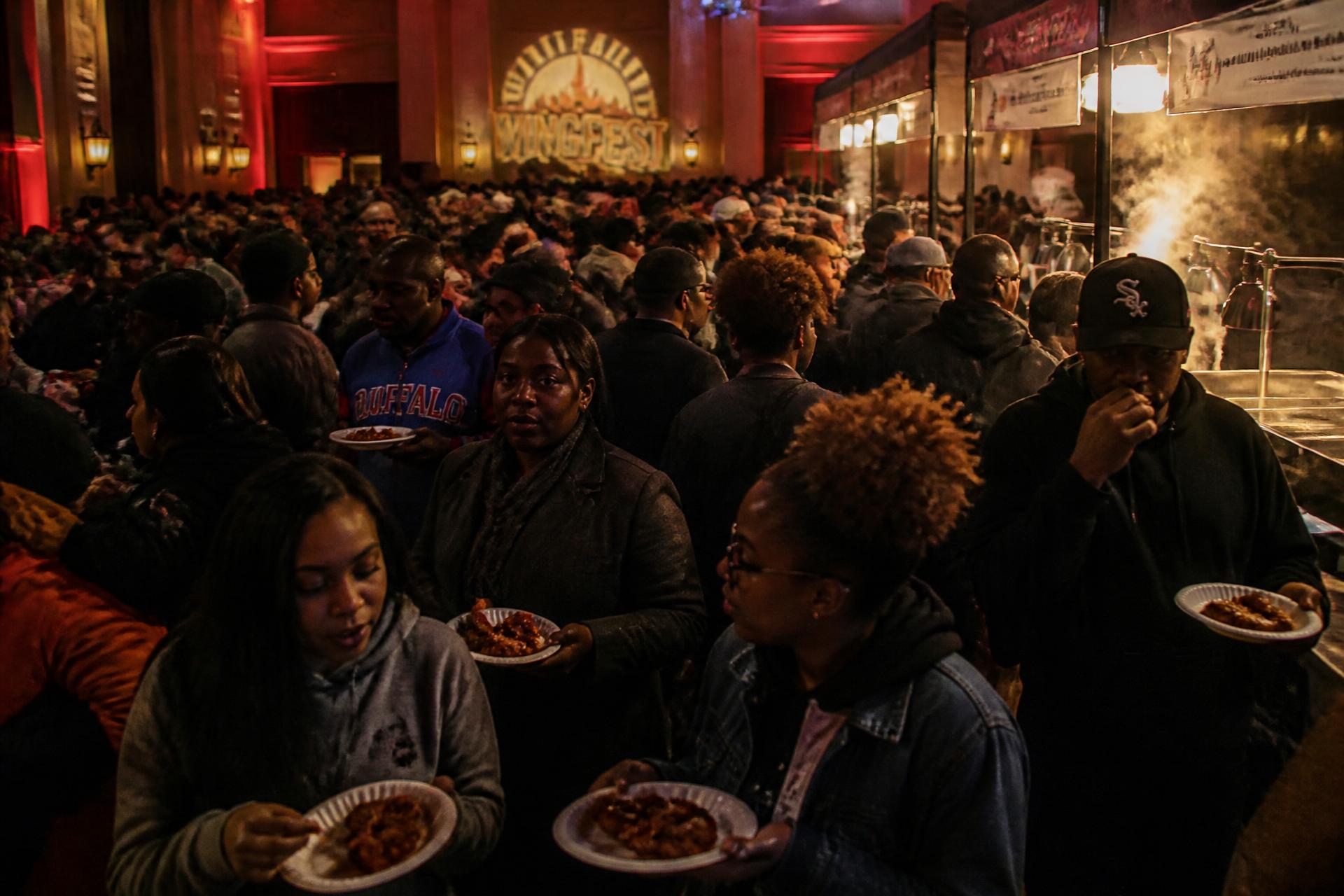 Guests holding plates of chicken wings at a packed Wing Wars event hall